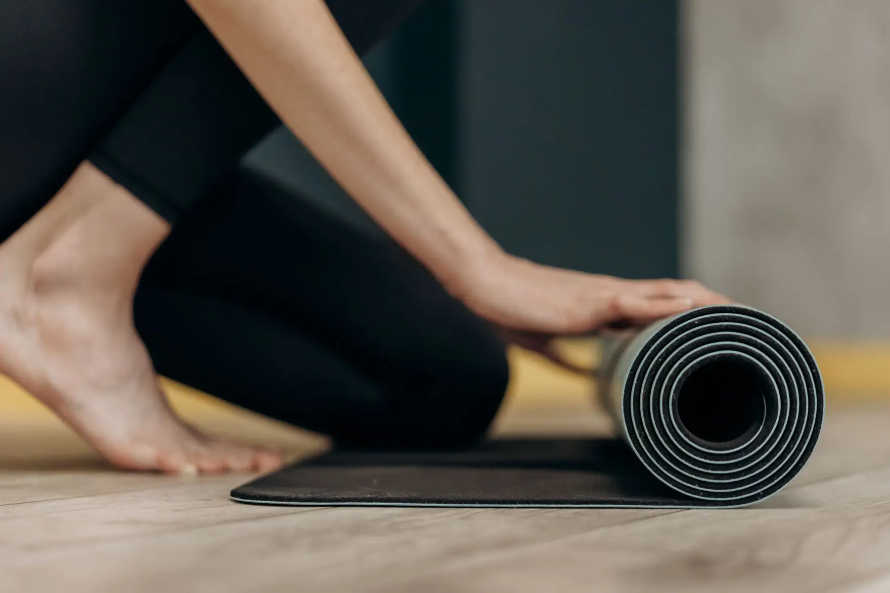 Frau rollt eine Yogamatte auf dem Holzboden aus